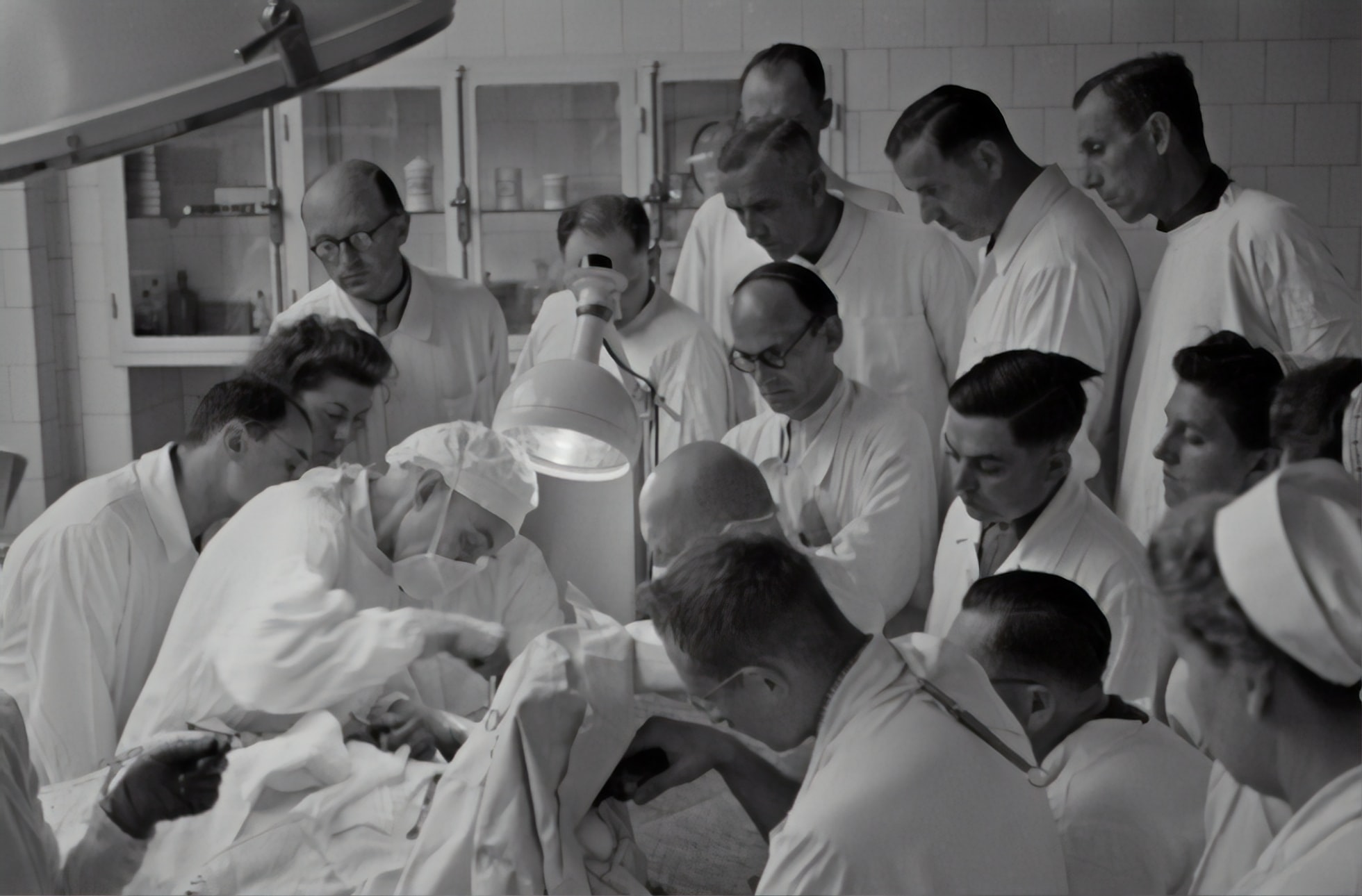 Old Image of a surgery with a dozen of people around the patient and watching