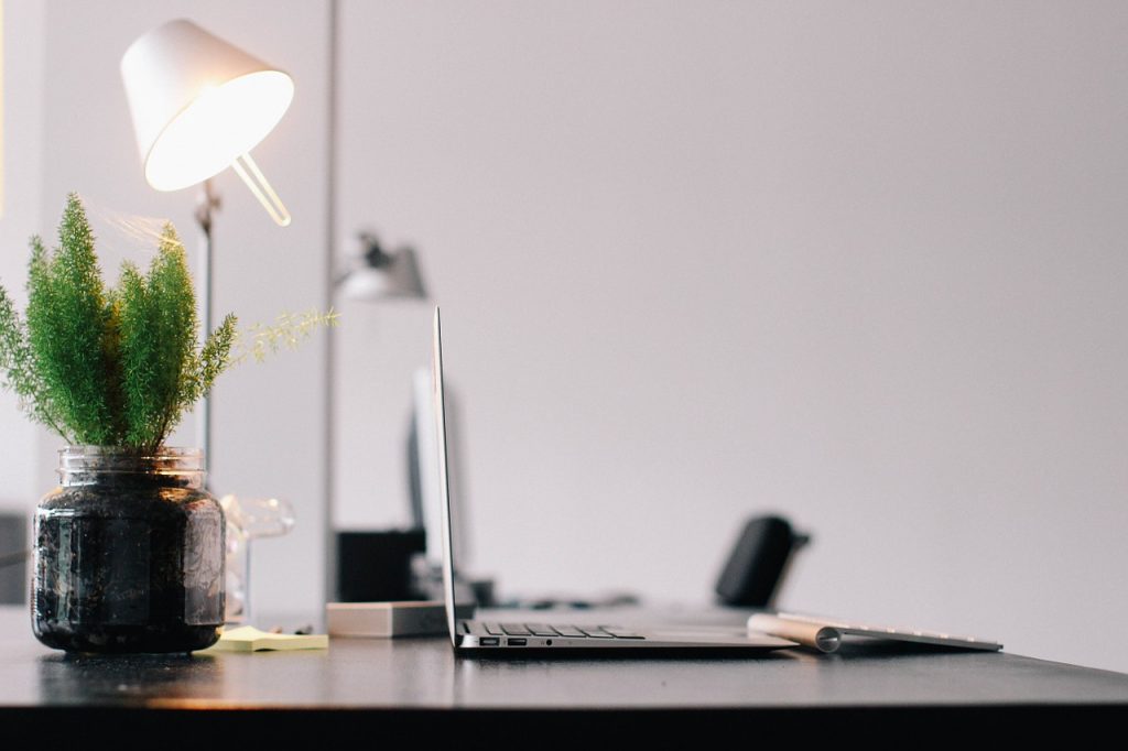 Image of an clean and modern desk with a laptop, lamp and a plant placed on it in a clinic