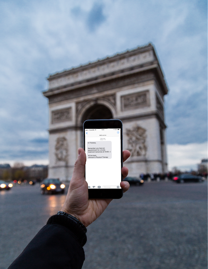 A hand holding a smartphone displaying a message. Message content is a reminder for an upcoming appointment.