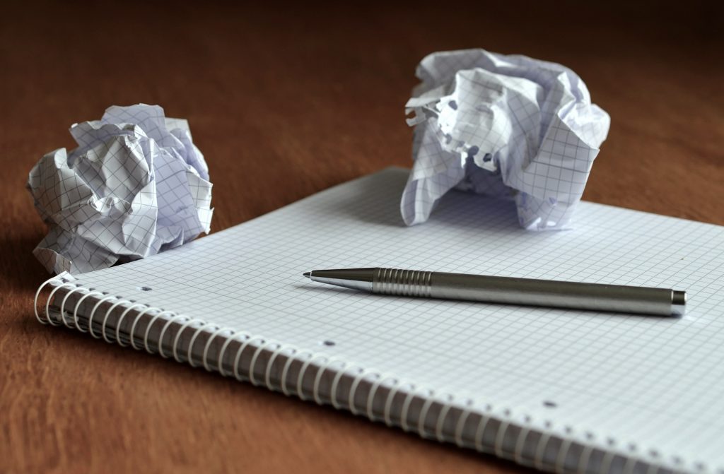 En notatbok med en penn og to krøllete papirer liggende ved siden av og ovenpå 