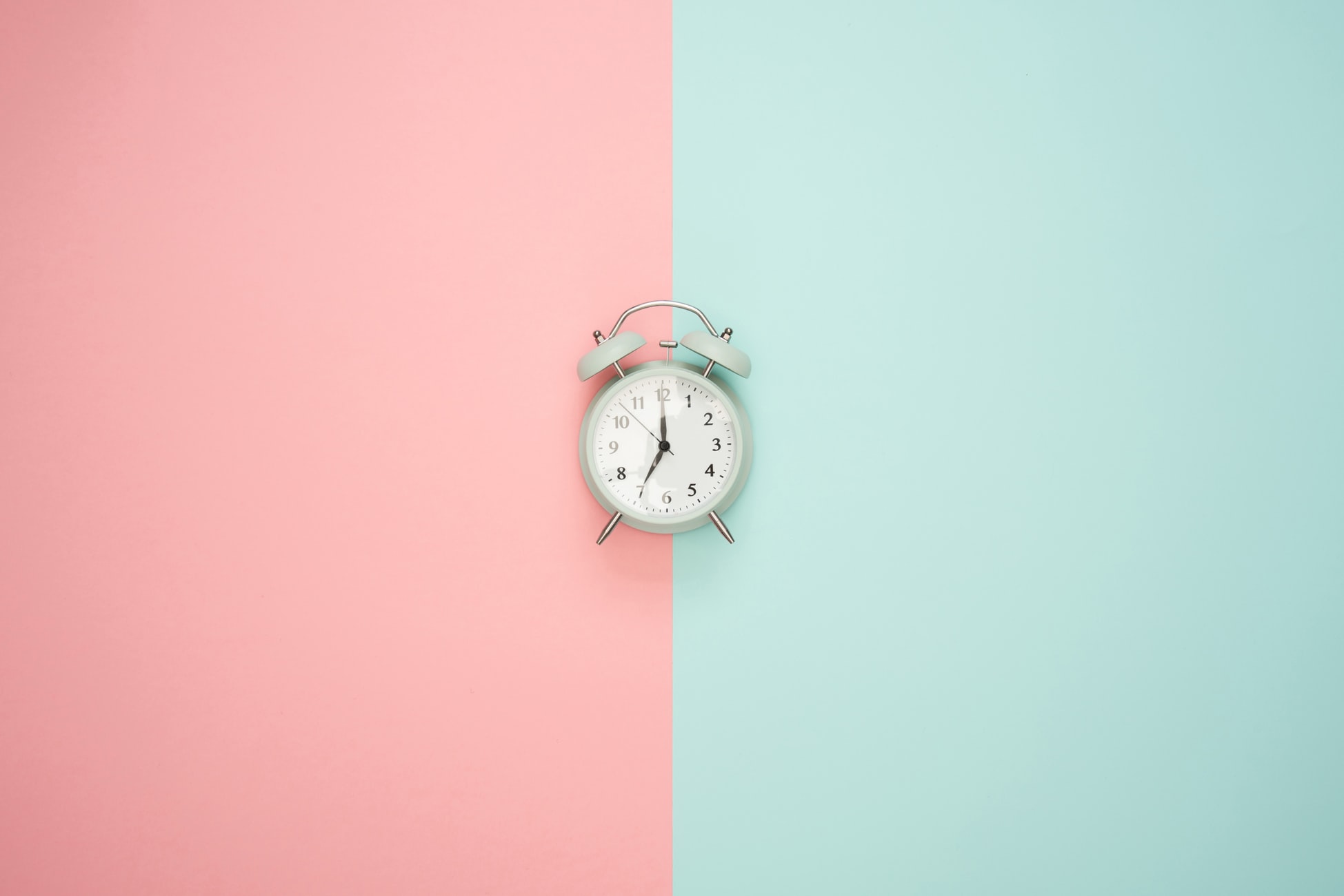Image of an old classic alarm clock on a pink and green background