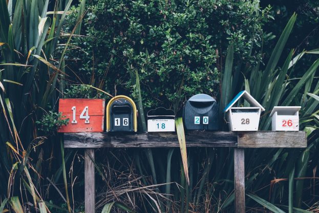 Forskjellige postkasser ved siden av hverandre foran en grønn skog