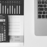 En pc, papir og kalkulator i sort-hvitt