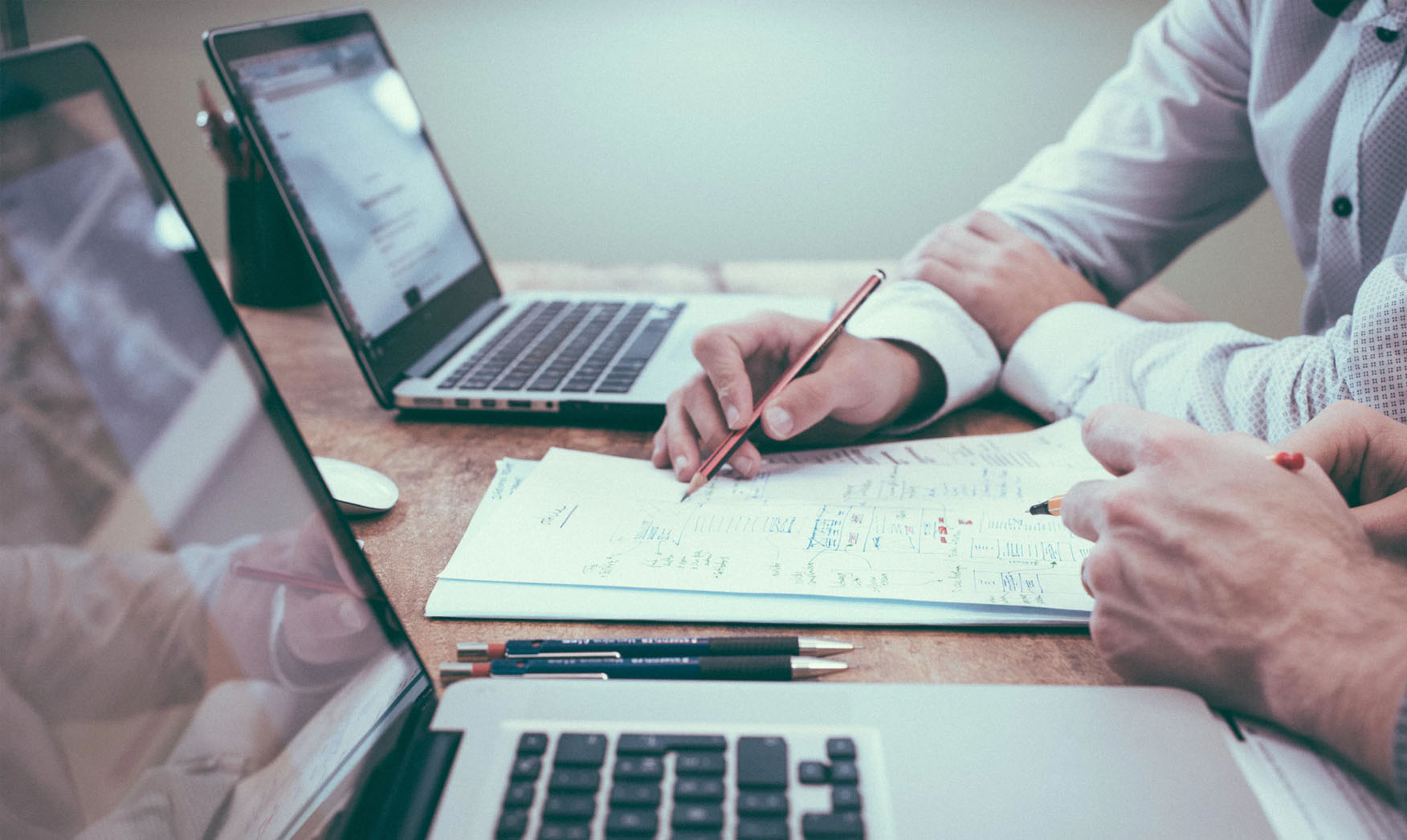 Two people with their laptops looking together at some notes and documents