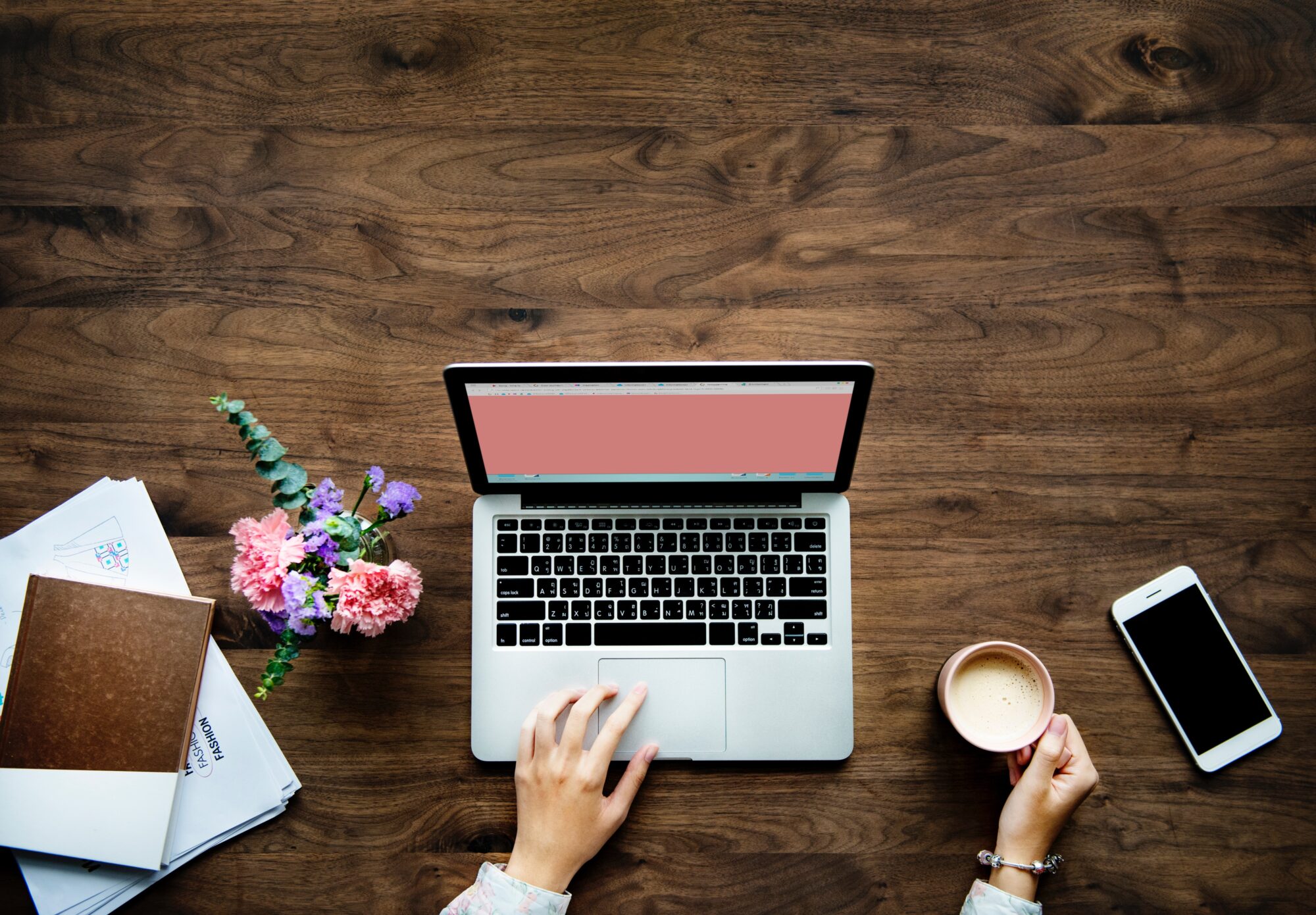 Kvinna sitter vid ett träbord med en öppen laptop och en kaffekopp i handen. 