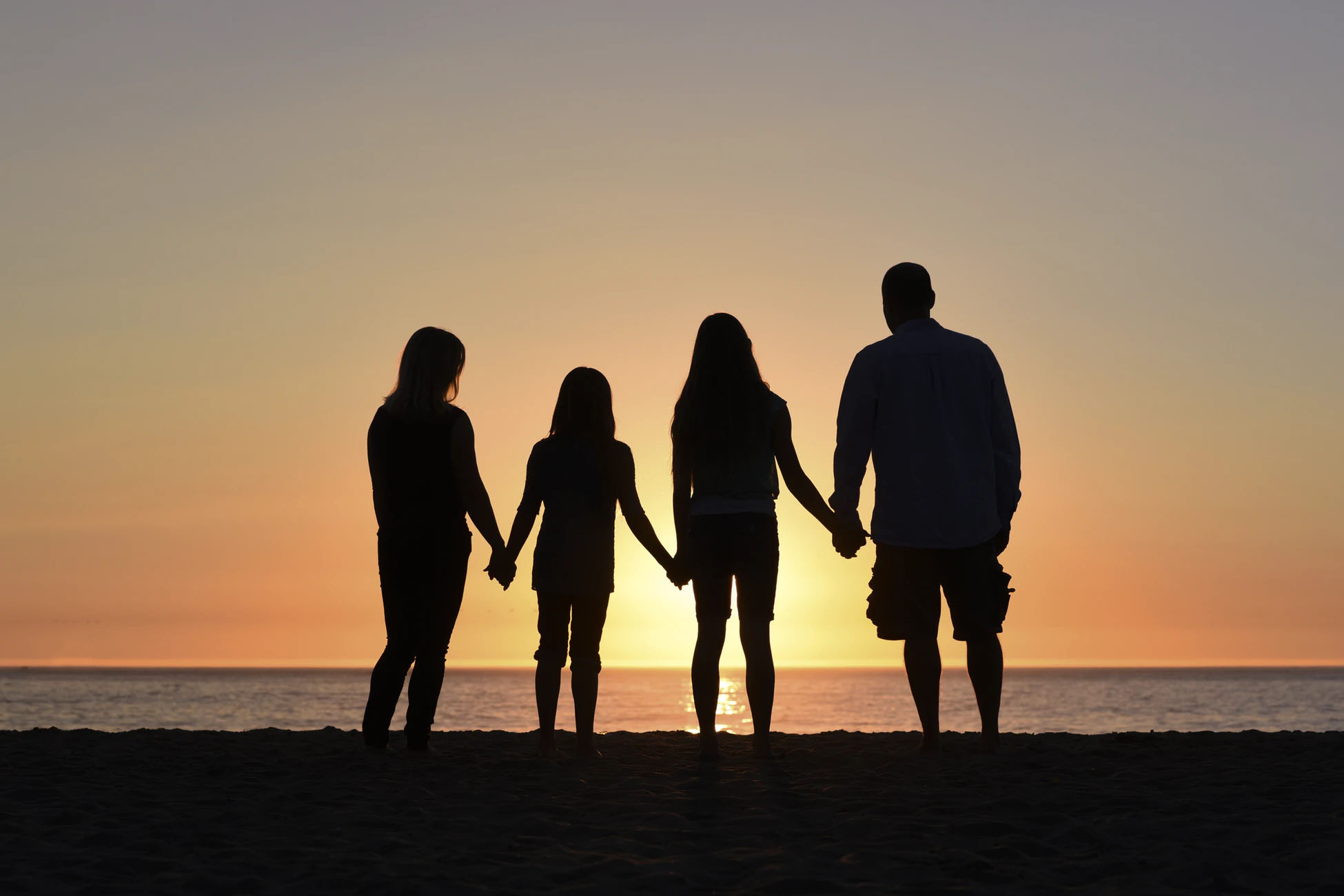 En familie som holder hender foran en solnedgang 