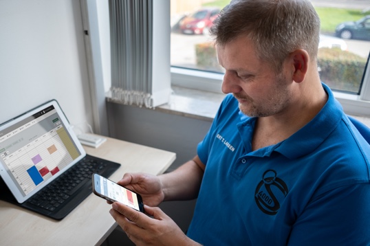 Man using his EasyPractice calendar on a smartphone in front of a laptop showing the same calendar