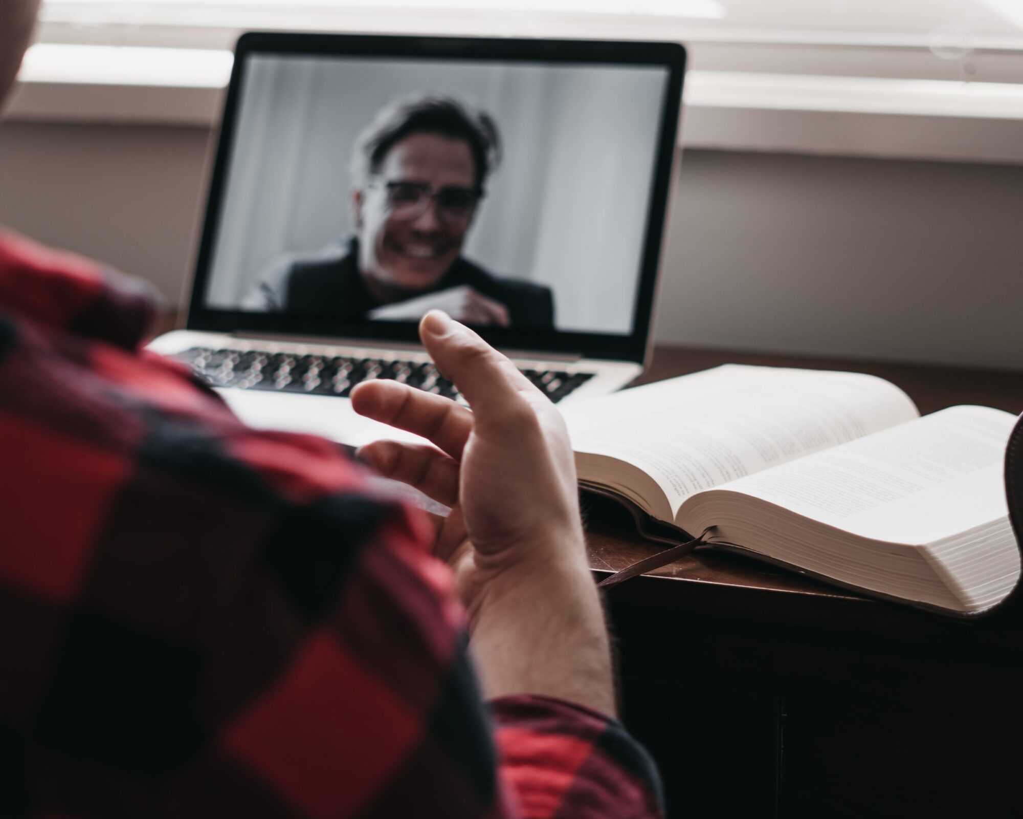 Man having an Online meeting via laptop and an open book is placed next to him