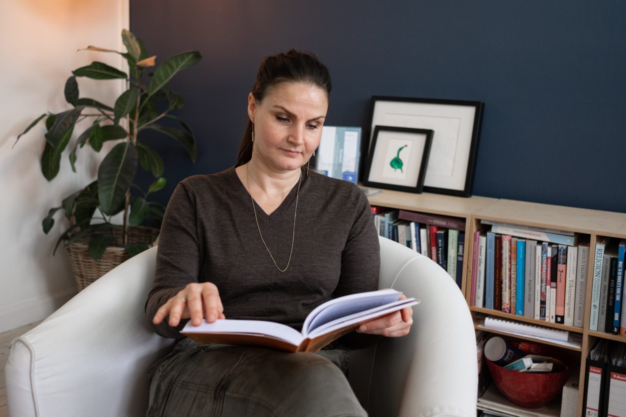 Lise sitter i en fåtölj i sitt hemmakontor och läser en bok. 