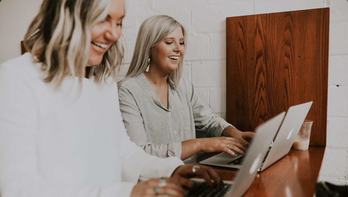 Two women in front of their laptops and smiling.