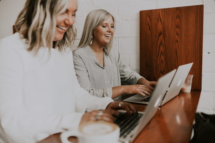 Two women in front of their laptops and smiling.