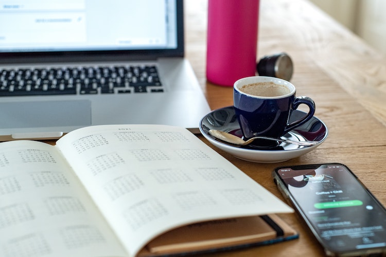 Image of a laptop, notebook, cup of coffee and a smartphone placed on a desk.