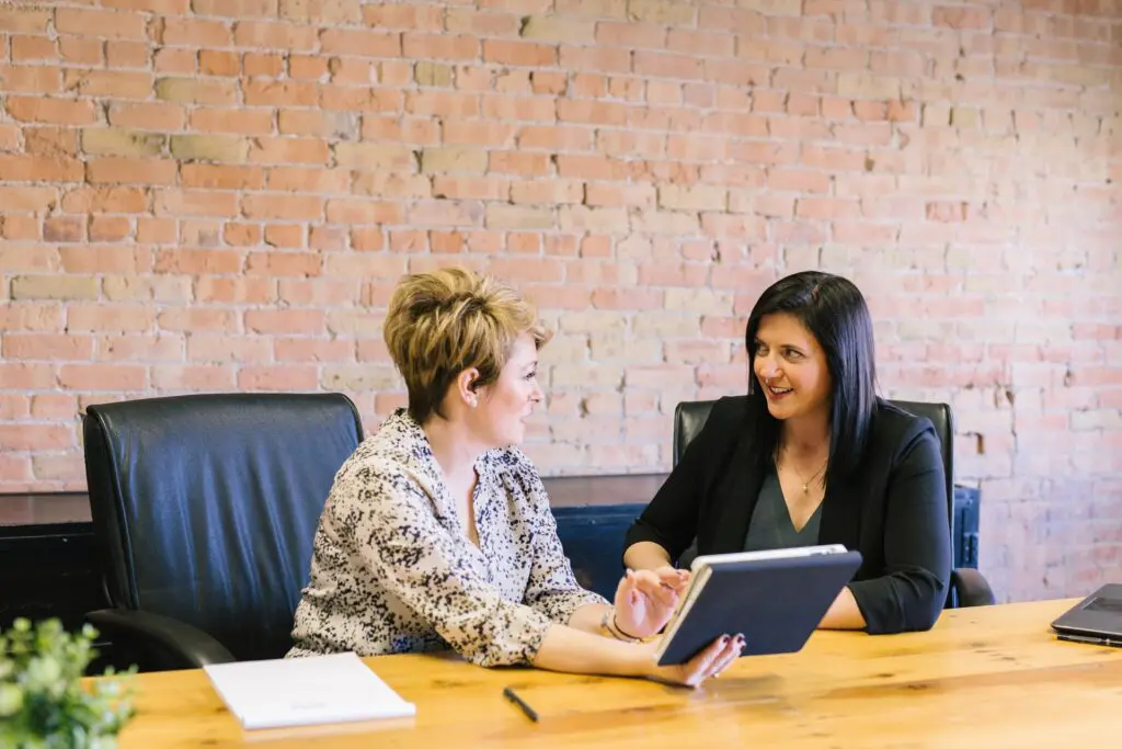 Two woman sitting on a desk and discussing a topic.