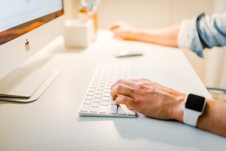 Man is sitting at a Mac computer with a keyboard and mouse.