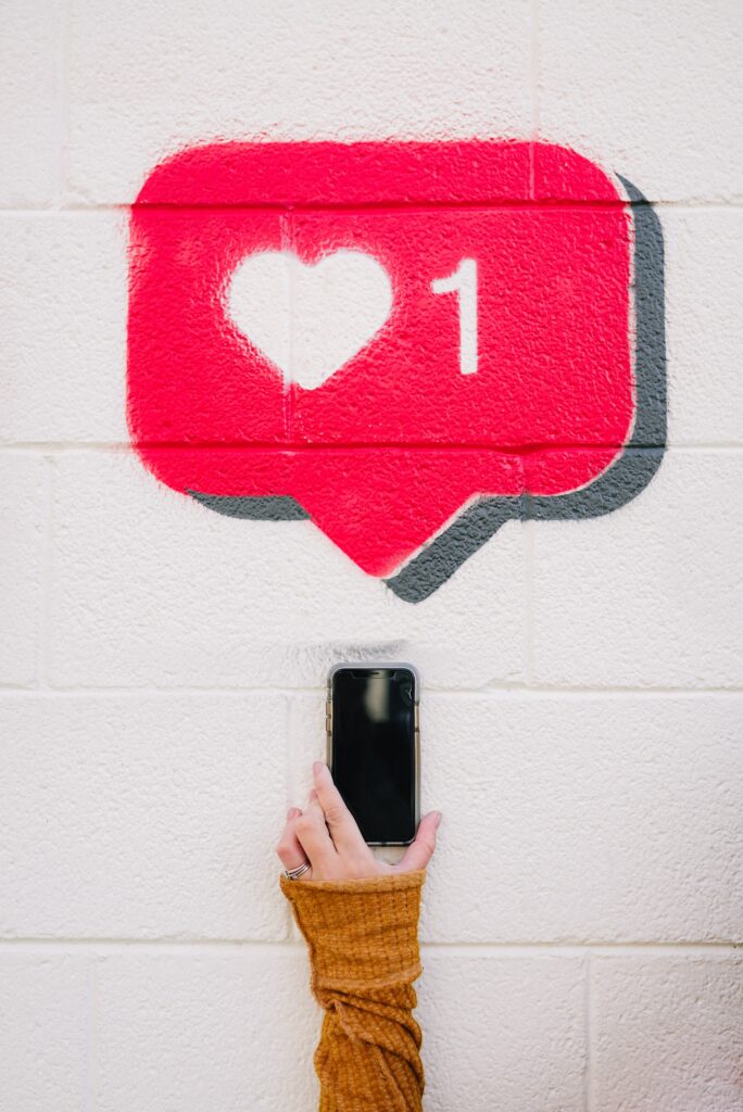 En illustrert "like" på en vegg med en hånd som holder en mobiltelefon under