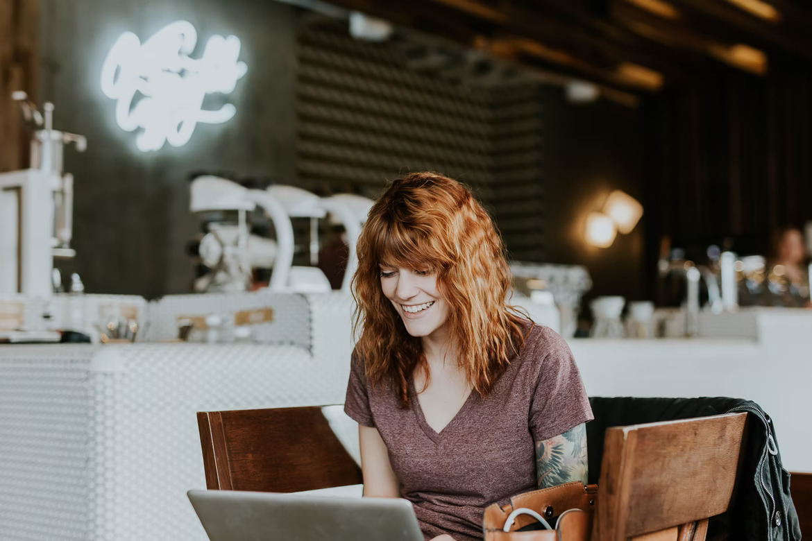 Redhead woman sitting on a wooden chair looking at the laptop on and smiling