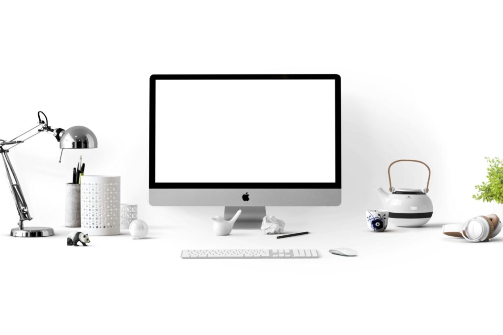 Image of a iMac, a desk lamp, a teapot and headphones placed on a white background.