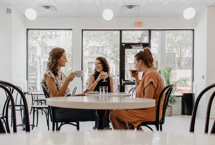 Tre damer som drikker kaffe over et bord i en cafe.