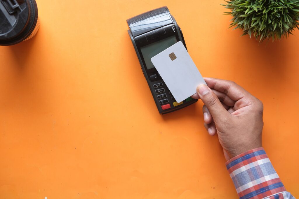 A hand is holding a debit card and is about to flash it on a card reader. 