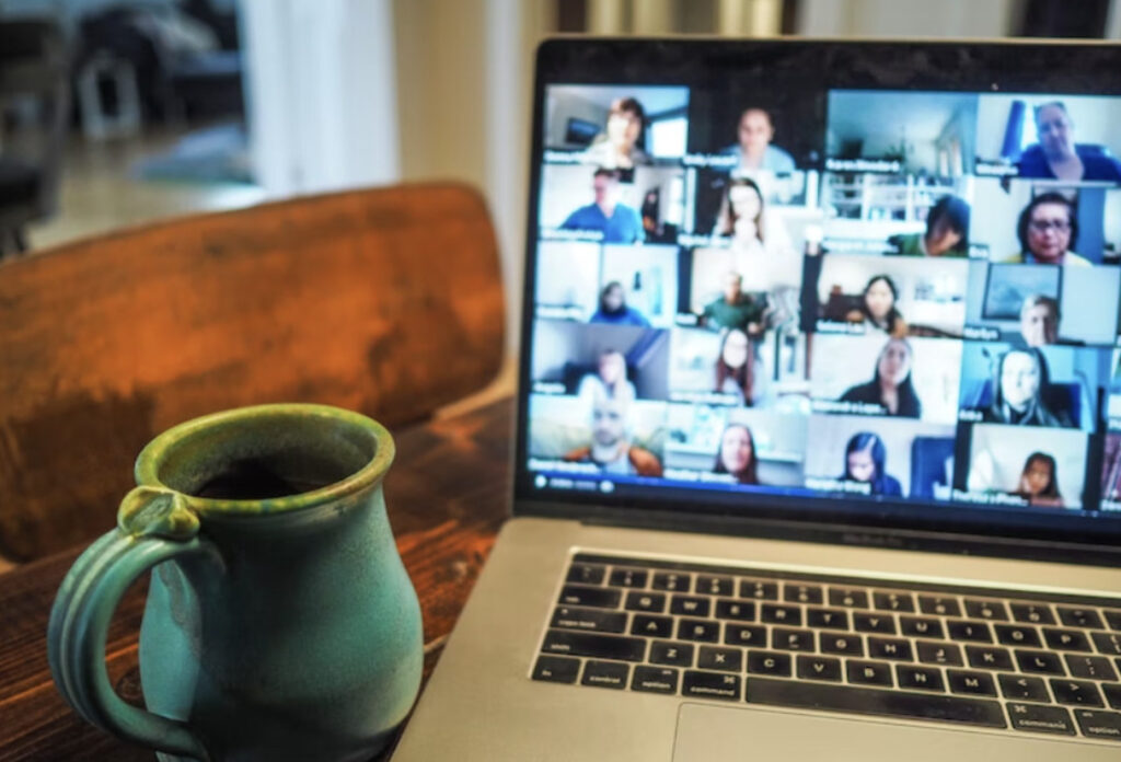 En pc-skjerm med et felles videooppkall i bakgrunnen og en kaffekopp på venstre side av pc'en