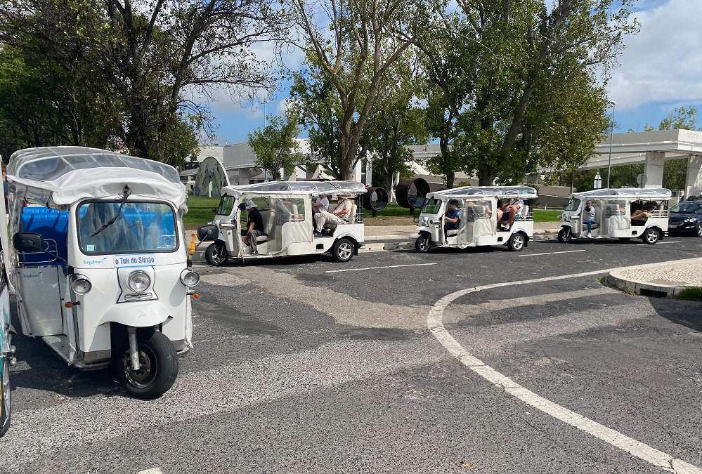 Four white tuk-tuks in a row on a paved road